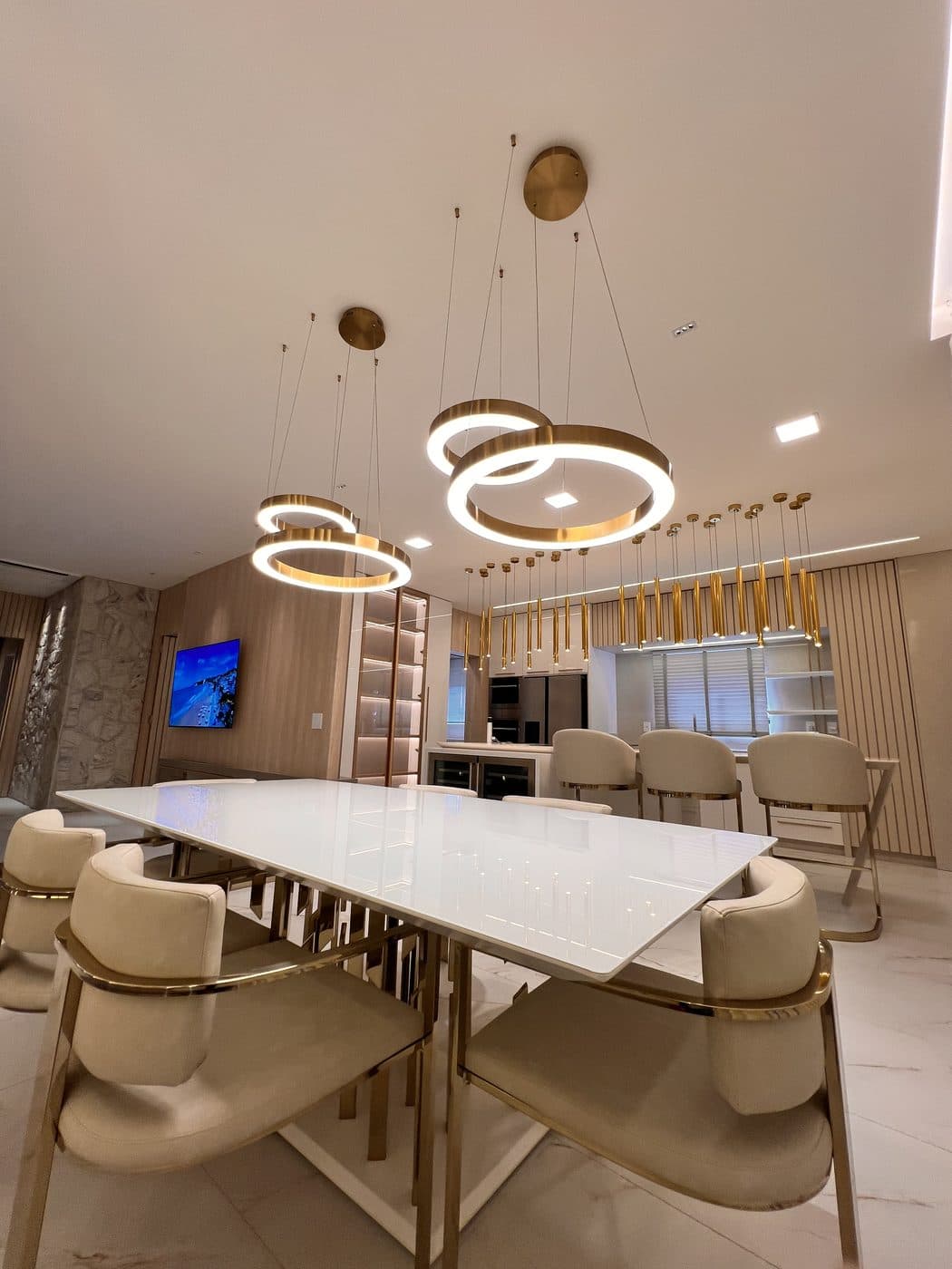 Sala de jantar com pendentes de anéis dourados e iluminação embutida no teto